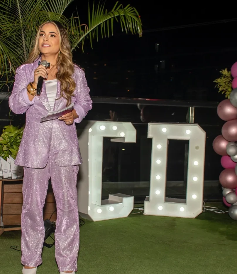 Jacque Americano no palco do Celebrate Day 2025, no rooftop, com as letras iluminadas CD